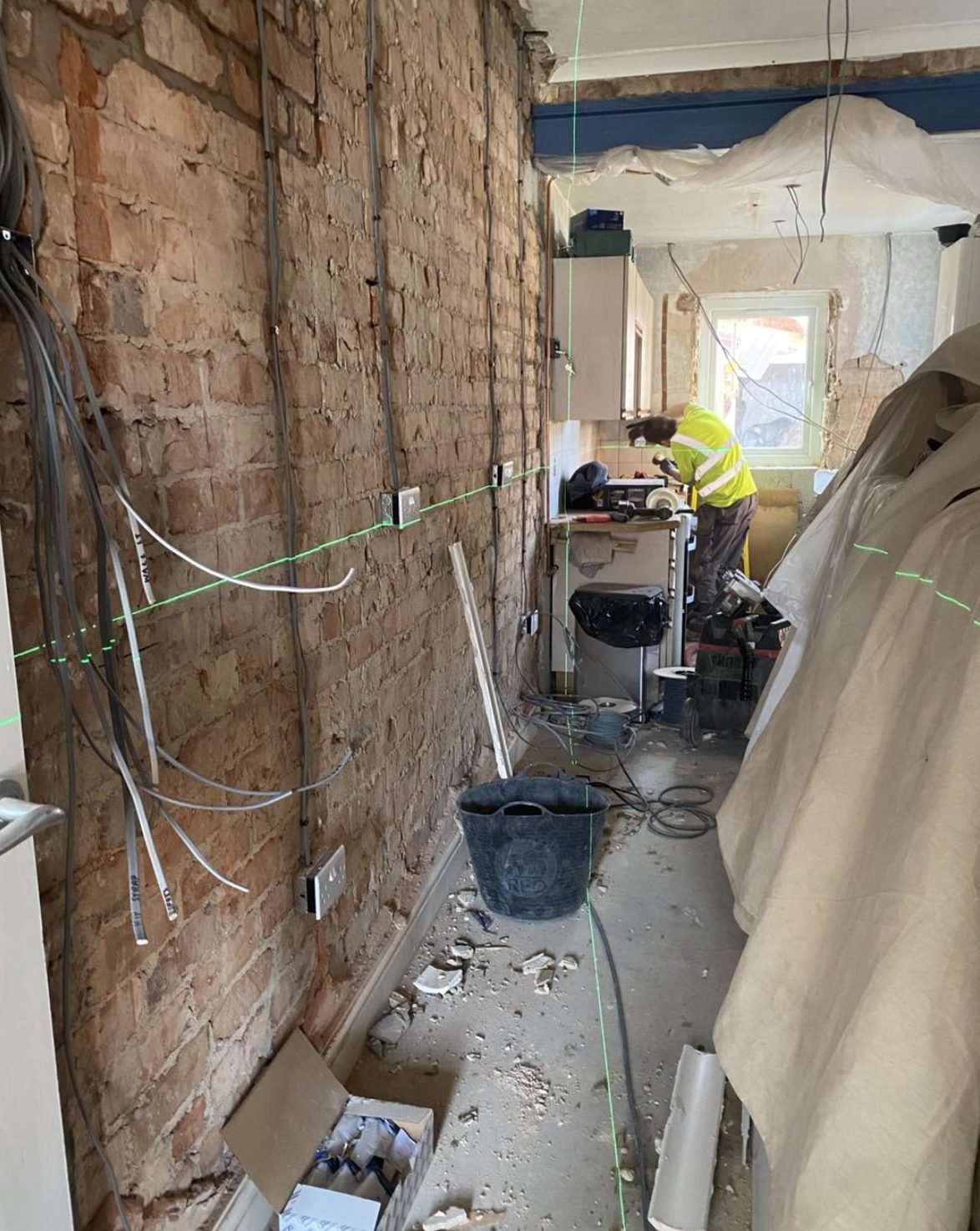 First fix rewire cables run down a stripped brick wall with a laser level line